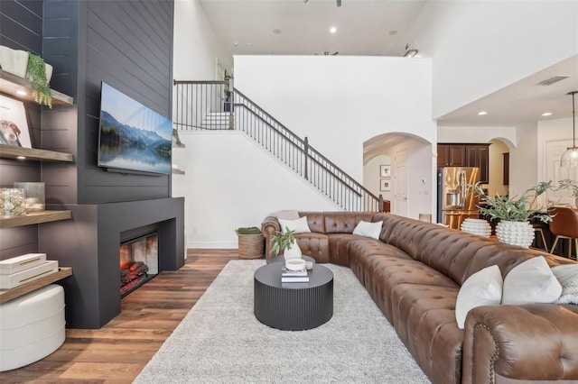 living room featuring a fireplace, arched walkways, wood finished floors, visible vents, and stairway