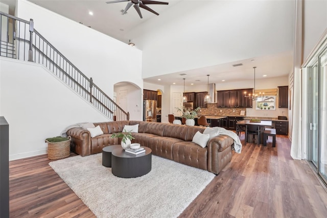 living area featuring ceiling fan with notable chandelier, a towering ceiling, wood finished floors, and arched walkways