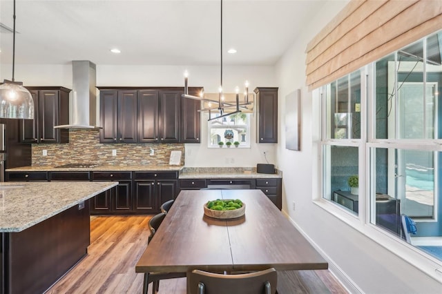 kitchen with wall chimney range hood, a chandelier, light wood-style flooring, stainless steel gas stovetop, and pendant lighting