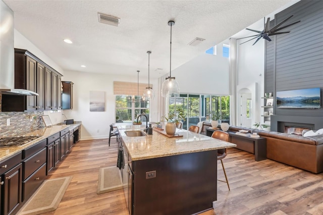 kitchen featuring ceiling fan, visible vents, stainless steel gas cooktop, a sink, and wall chimney exhaust hood