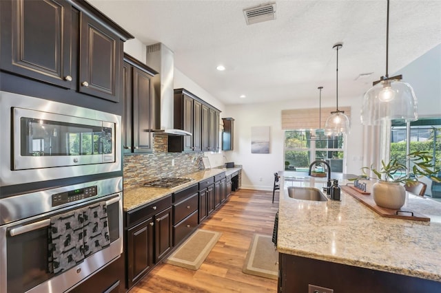 kitchen featuring dark brown cabinets, light wood-type flooring, a sink, appliances with stainless steel finishes, and backsplash
