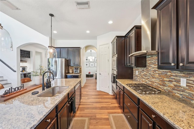 kitchen featuring a sink, arched walkways, wall chimney exhaust hood, stainless steel appliances, and visible vents