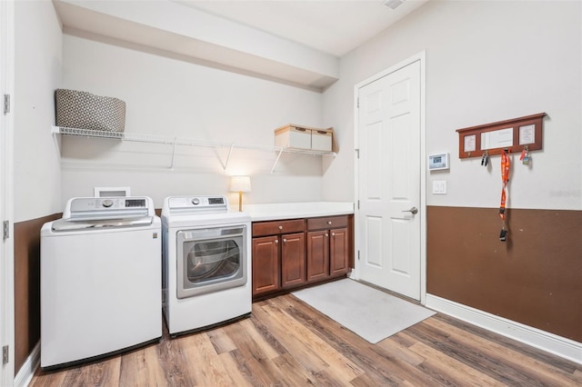 laundry area featuring baseboards, light wood-style flooring, cabinet space, and washing machine and dryer