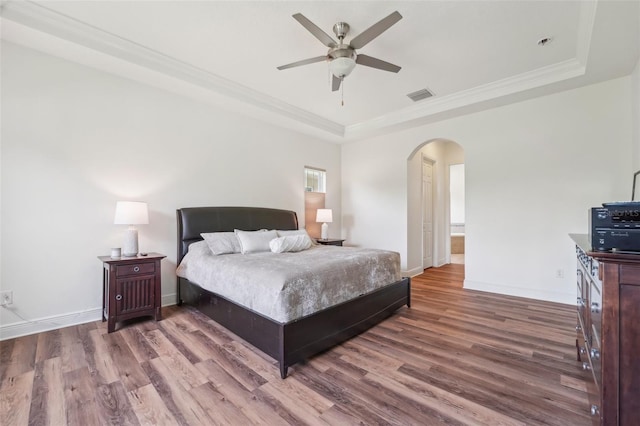bedroom featuring a raised ceiling, arched walkways, wood finished floors, and visible vents