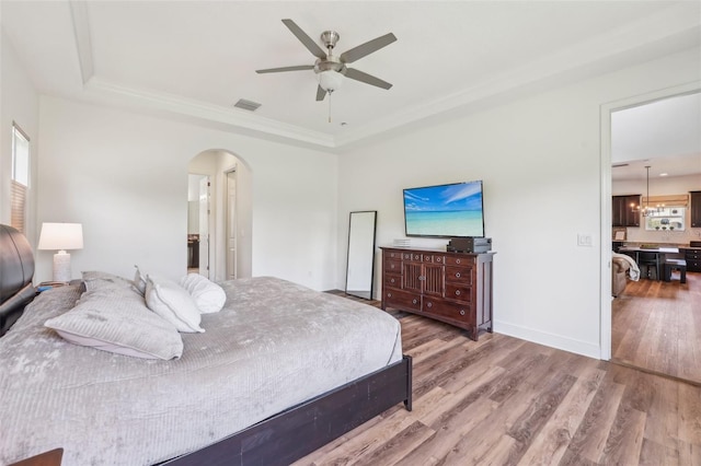 bedroom with a raised ceiling, arched walkways, wood finished floors, and visible vents