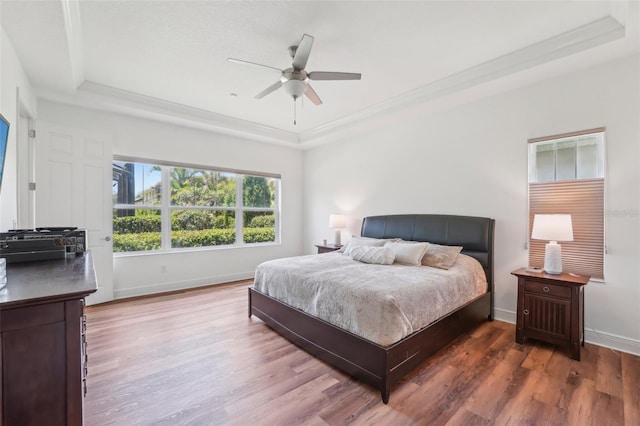 bedroom with a raised ceiling, a ceiling fan, baseboards, wood finished floors, and ornamental molding
