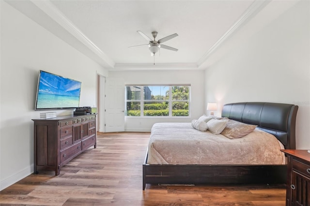 bedroom with crown molding, a raised ceiling, baseboards, and light wood finished floors