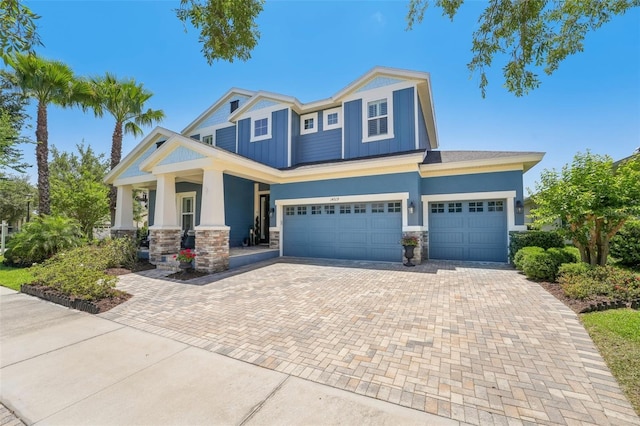 craftsman inspired home featuring an attached garage, stone siding, stucco siding, decorative driveway, and covered porch