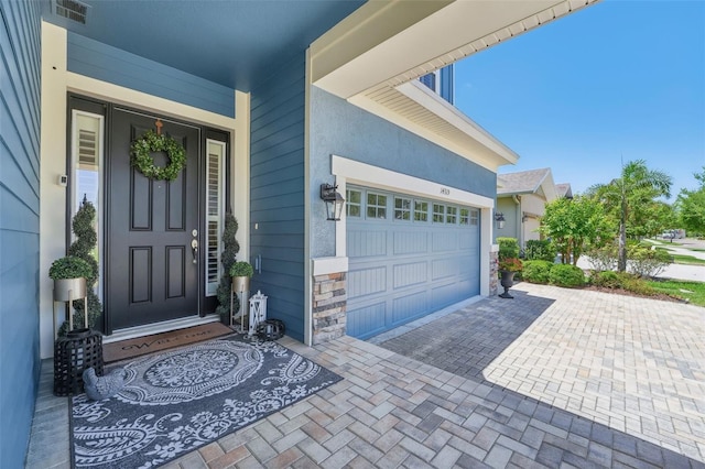 doorway to property featuring visible vents, an attached garage, decorative driveway, and stone siding