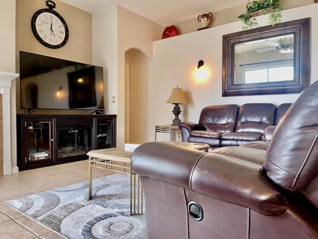 tiled living room featuring arched walkways and a glass covered fireplace