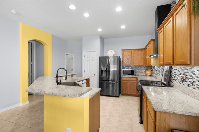 kitchen featuring a sink, arched walkways, stainless steel appliances, tasteful backsplash, and a center island with sink