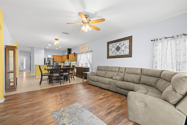 living area featuring ceiling fan, visible vents, baseboards, and light wood finished floors