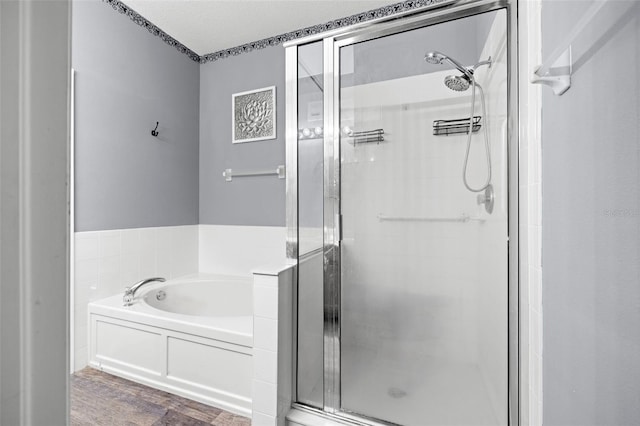 full bathroom featuring a stall shower, a bath, and wood finished floors