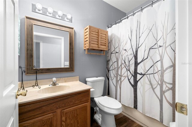 bathroom with toilet, curtained shower, wood finished floors, and vanity