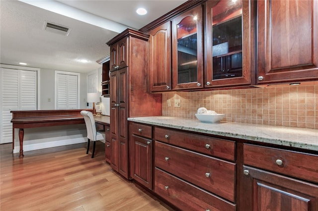 14820 Rue De Bayonne Unit 208, Clearwater, FL 33762 - kitchen with visible vents, built in desk, tasteful backsplash, and light wood-type flooring