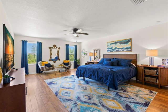 bedroom with a textured ceiling, ceiling fan, visible vents, and wood finished floors
