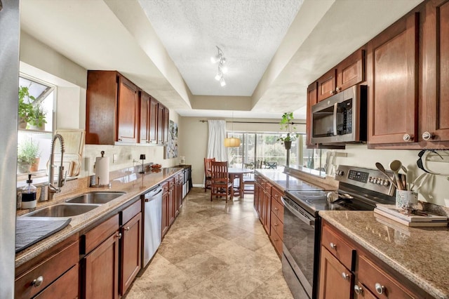 kitchen featuring a sink, stone counters, appliances with stainless steel finishes, and a tray ceiling