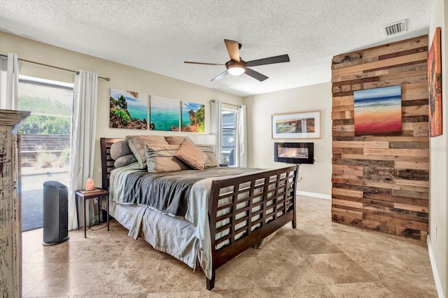 bedroom featuring wooden walls, a textured ceiling, visible vents, and multiple windows