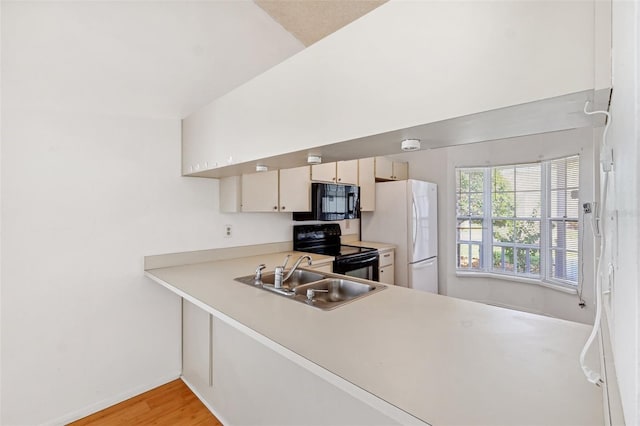 kitchen with black appliances, a sink, light countertops, baseboards, and light wood finished floors
