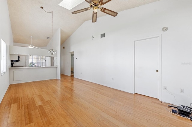 unfurnished living room featuring ceiling fan, high vaulted ceiling, light wood-type flooring, a skylight, and a chandelier
