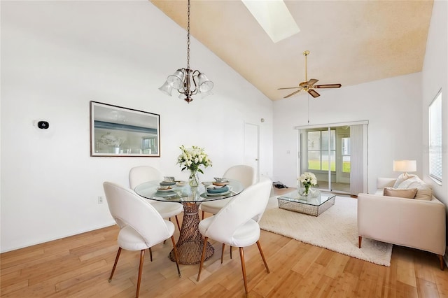 dining area featuring high vaulted ceiling, a skylight, light wood-style flooring, a ceiling fan, and a chandelier