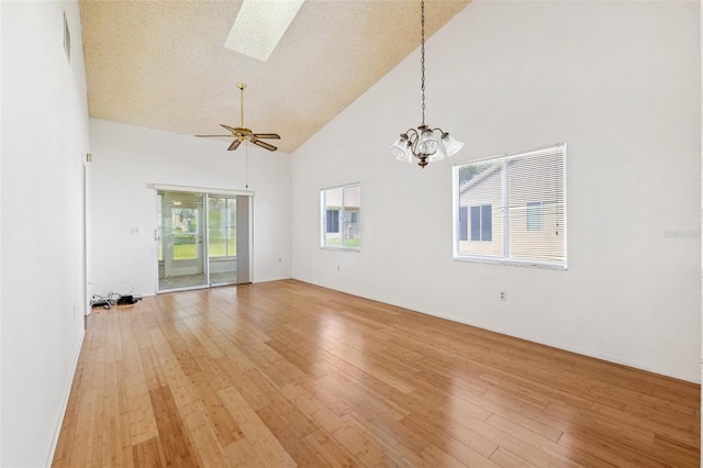 spare room with high vaulted ceiling, light wood-style flooring, a skylight, a chandelier, and a ceiling fan
