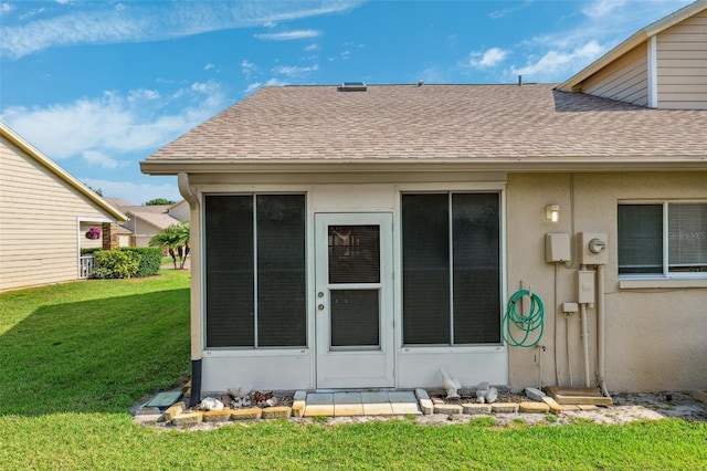 rear view of property with roof with shingles, a lawn, and stucco siding