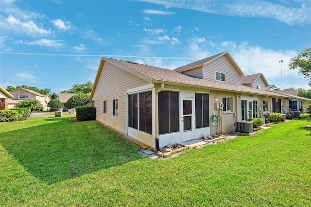 back of property with a sunroom, a lawn, a shingled roof, and central AC