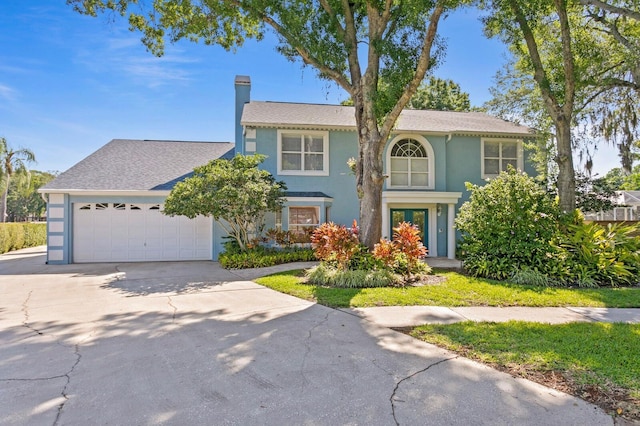 traditional-style home featuring an attached garage, stucco siding, a chimney, and driveway