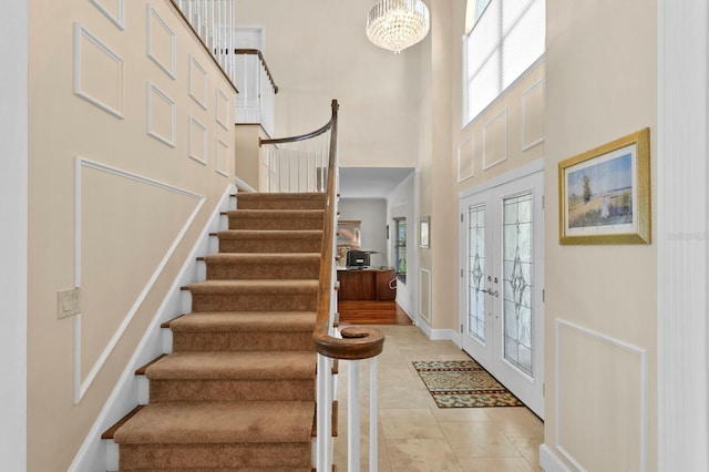 entryway featuring a towering ceiling, light tile patterned floors, baseboards, a chandelier, and stairs