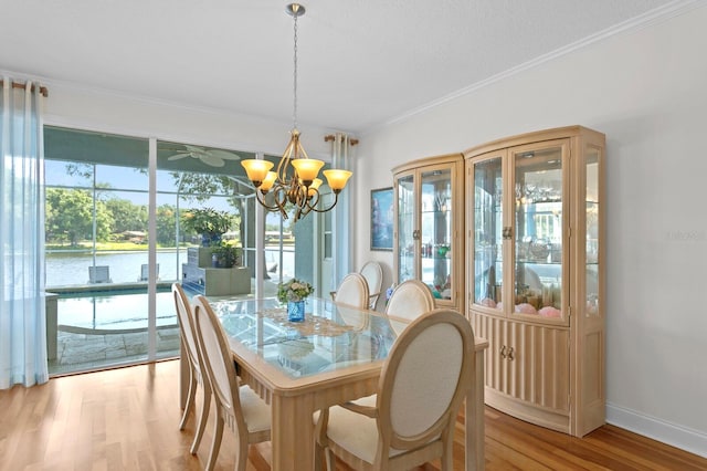 dining space featuring baseboards, light wood finished floors, a chandelier, a water view, and ornamental molding