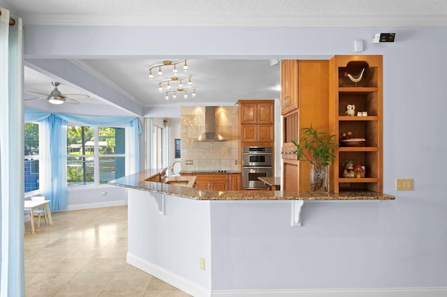 kitchen featuring brown cabinets, a kitchen breakfast bar, stainless steel double oven, and wall chimney exhaust hood