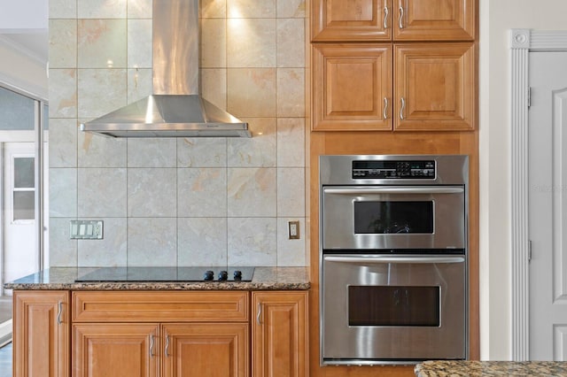kitchen with backsplash, black electric cooktop, double oven, stone counters, and wall chimney exhaust hood