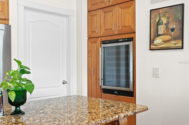 kitchen with beverage cooler, brown cabinets, and light stone countertops