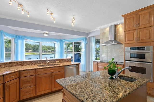 kitchen with a sink, wall chimney exhaust hood, dark stone counters, and stainless steel appliances