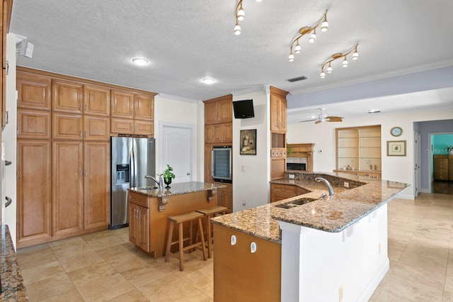 kitchen featuring a kitchen breakfast bar, crown molding, appliances with stainless steel finishes, a center island with sink, and a sink