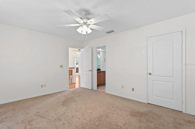 unfurnished bedroom with a ceiling fan, visible vents, baseboards, ensuite bathroom, and light carpet
