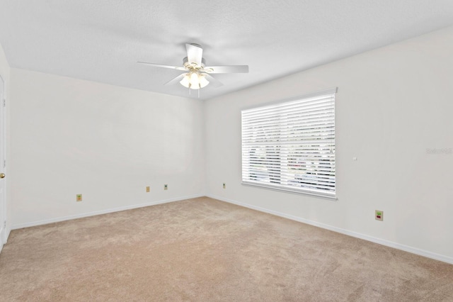 empty room with light colored carpet, a ceiling fan, and baseboards