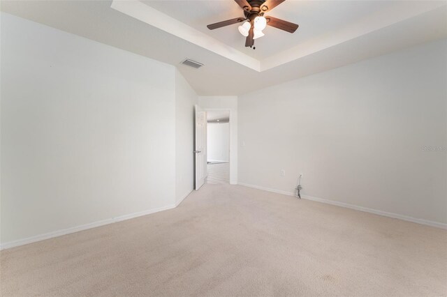 spare room featuring light colored carpet, a ceiling fan, baseboards, a tray ceiling, and visible vents