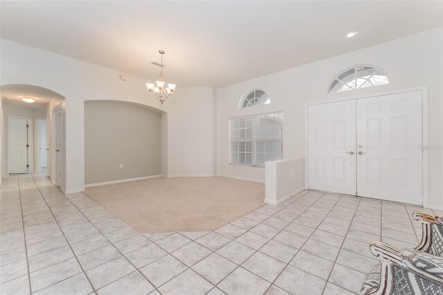 foyer featuring arched walkways, light tile patterned floors, baseboards, a notable chandelier, and light carpet