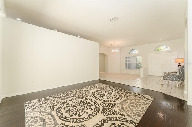 unfurnished living room featuring an inviting chandelier, arched walkways, hardwood / wood-style floors, baseboards, and visible vents