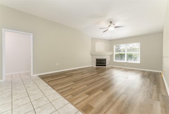 unfurnished living room with baseboards, ceiling fan, light wood-style flooring, and a tile fireplace