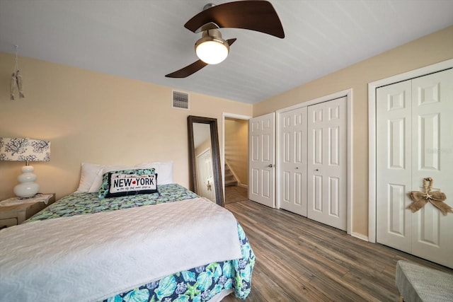 bedroom with visible vents, two closets, wood finished floors, baseboards, and ceiling fan