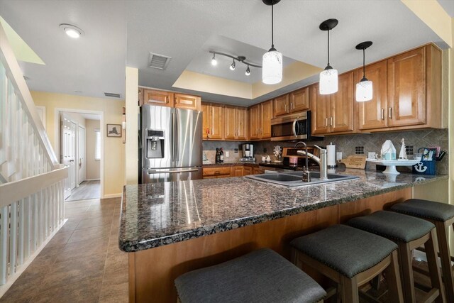 kitchen featuring visible vents, a peninsula, a raised ceiling, brown cabinets, and appliances with stainless steel finishes
