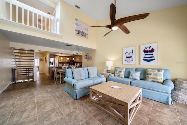 living room featuring visible vents, baseboards, ceiling fan, and a high ceiling