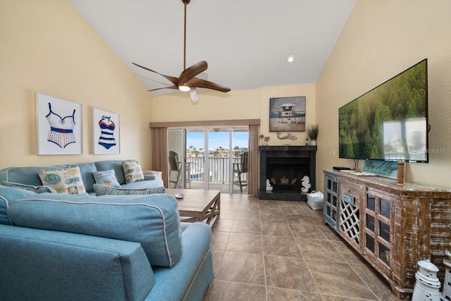 living area with tile patterned flooring, a fireplace with raised hearth, ceiling fan, and high vaulted ceiling