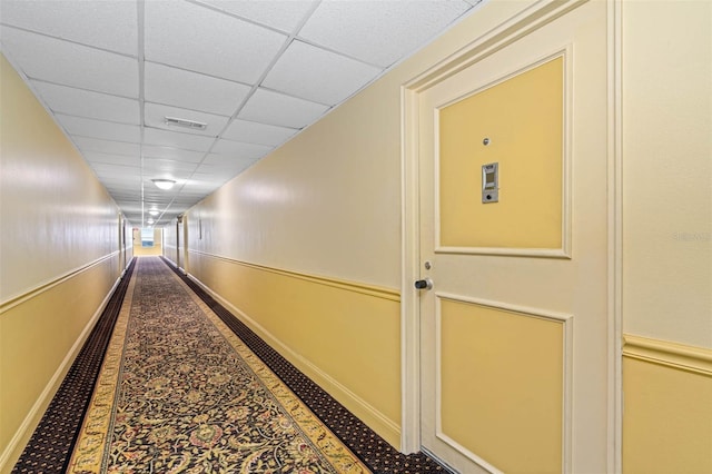 hall with baseboards, visible vents, and a paneled ceiling