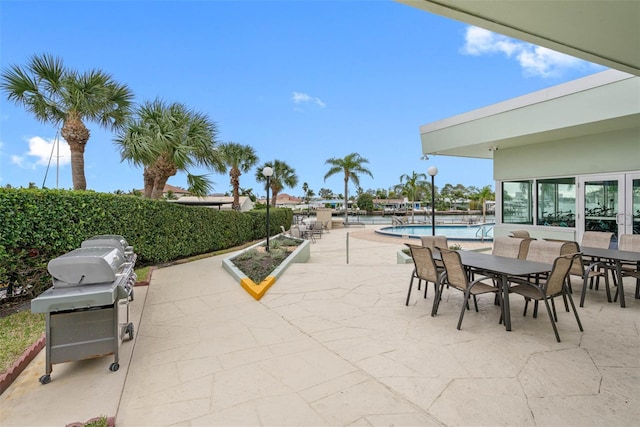 view of patio with a community pool, outdoor dining area, and a grill