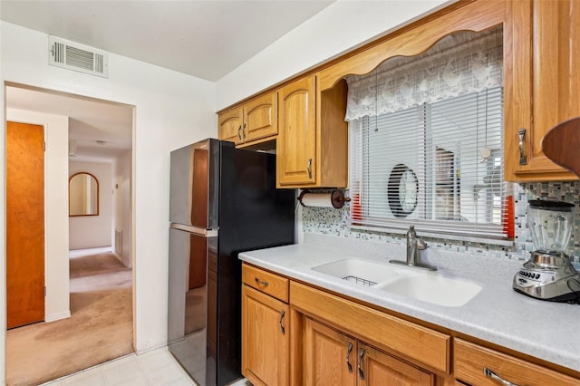 kitchen featuring freestanding refrigerator, visible vents, a sink, brown cabinets, and light countertops