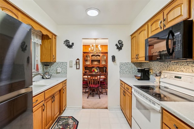 kitchen with a sink, freestanding refrigerator, electric range, a notable chandelier, and black microwave